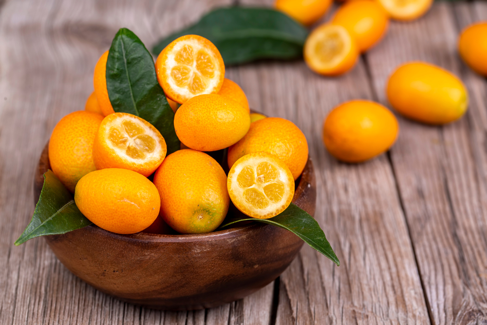 Un bol de lemn cu fructe de kumquat și frunze.