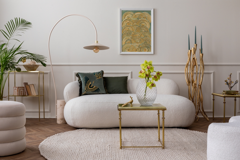 Living amenajat cu mobilier art deco, precum canapea cu margini rotunjite, măsuță de cafea, accesorii și corp de iluminat cu strucută metalică aurie, tablou cu motive art deco în nuanțe de galben.