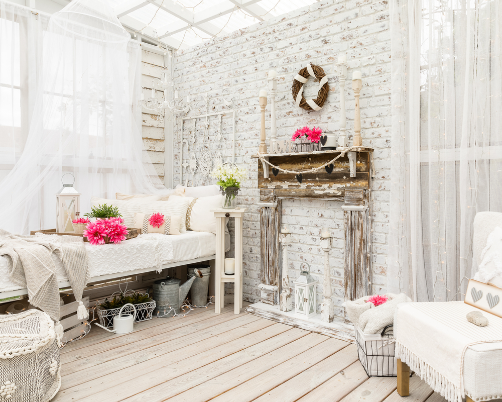 O cameră la casă în stilul shabby chic cu țesături fluide albe, mobilier și decorațiuni din lemn vechi și bujori roz proaspeți.