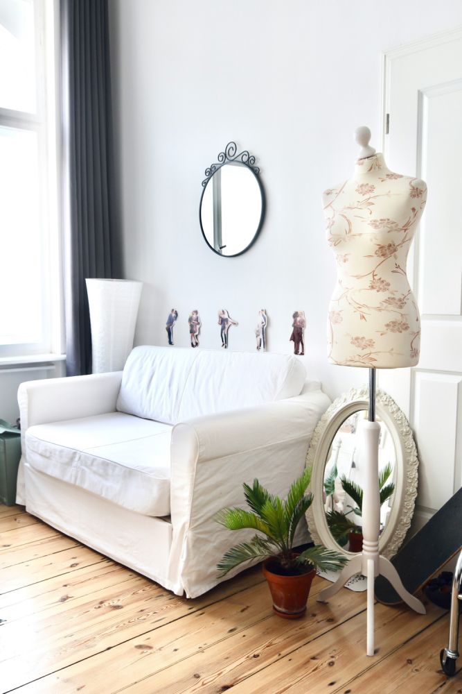 Un colțt de living cu elemente din stilul shabby chic, precum canapea albă, oglinzi ovale cu rame din fier sau lemn și imprimeuri florale.