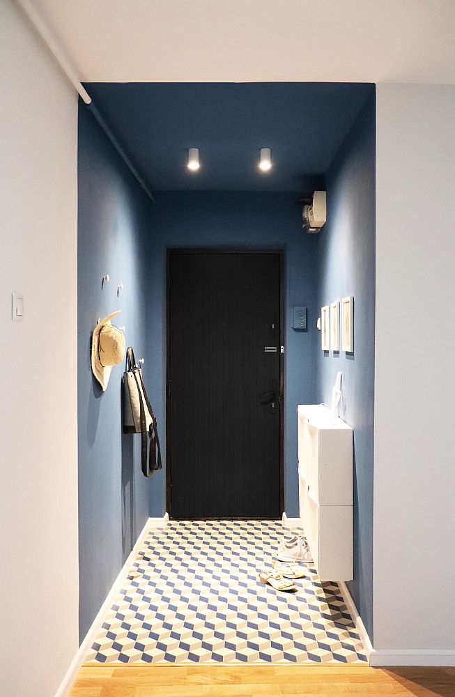 Un hol cu pereți de un albastru fad închis, spoturi de lumină cu led pe tavan și podea cu lunoleum cu modele geometrice alb și negru
