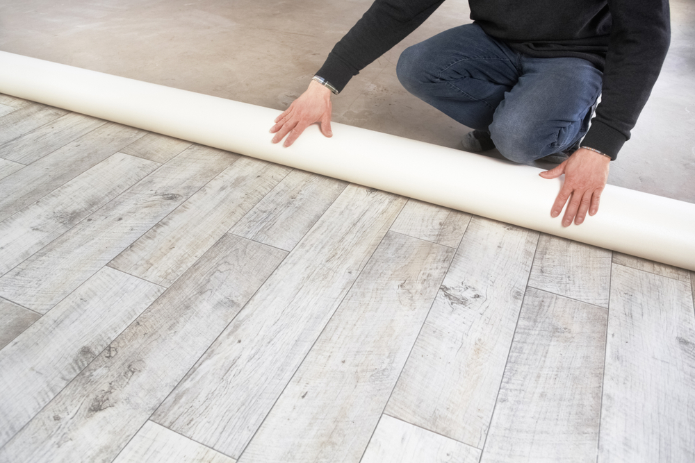 Mâini de bîrbat instalează o rolă de pardoseală din PVC cu aspect de parchet laminat gri
