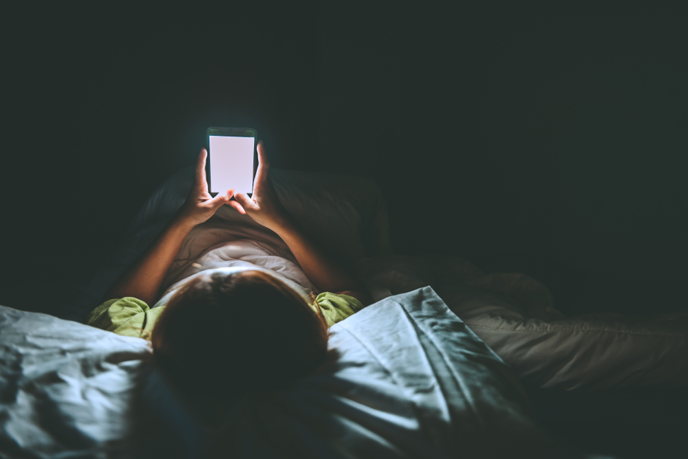 O femeie butonează telefonul pe întuneric în pat