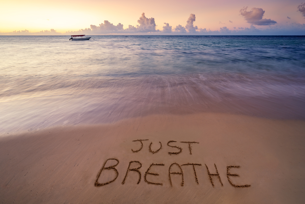 Marea la apus, iar pe nisip scris Just Breathe (doar respiră) - concept pentru respirație liniștitoare