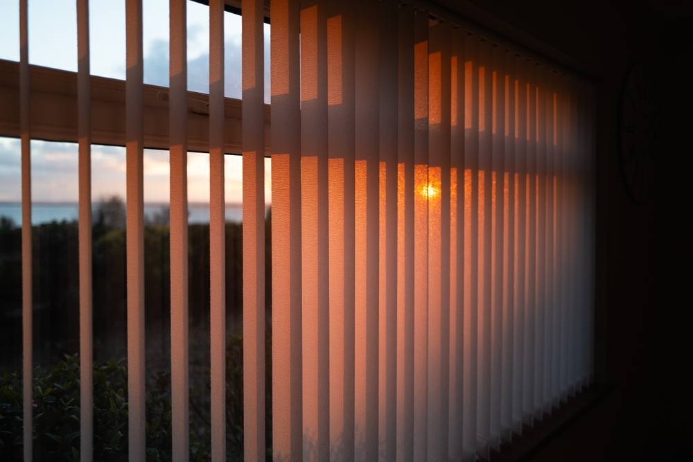 Jaluzele verticale portocalii la geam, în lumina finalului de apus.