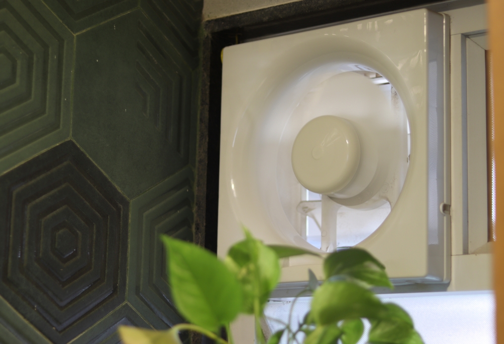 ventilator de baie pus in functiune intr-o amenajare cu faianta verde si plante