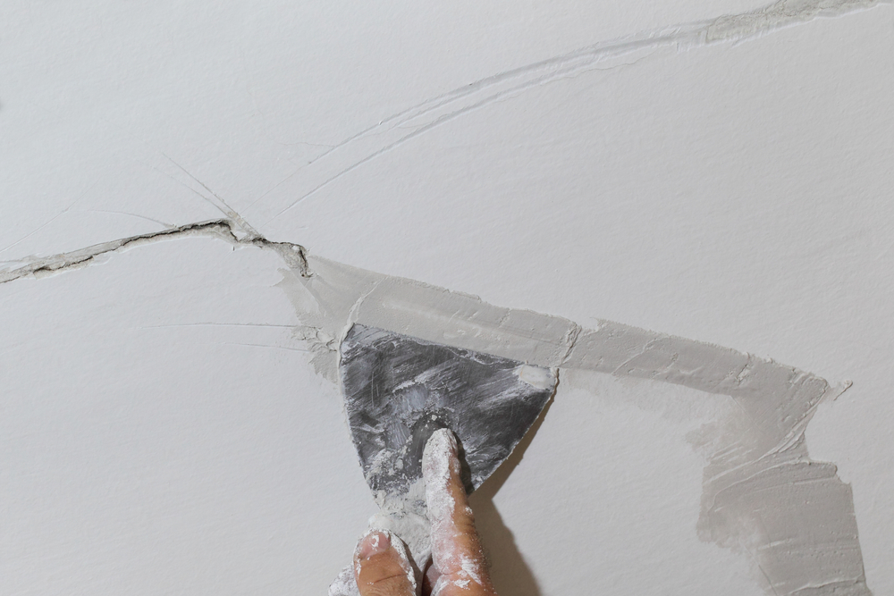 reparatie fisura crapatura perete cu chit de cutit aplicat cu un spaclu pe un zid alb
