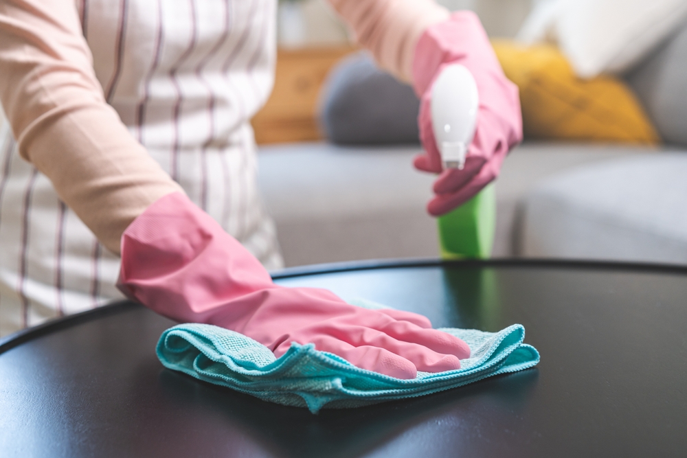 curatare praf de pe suprafetele cu lavete din microfibre de catre femeie cu manusi roz