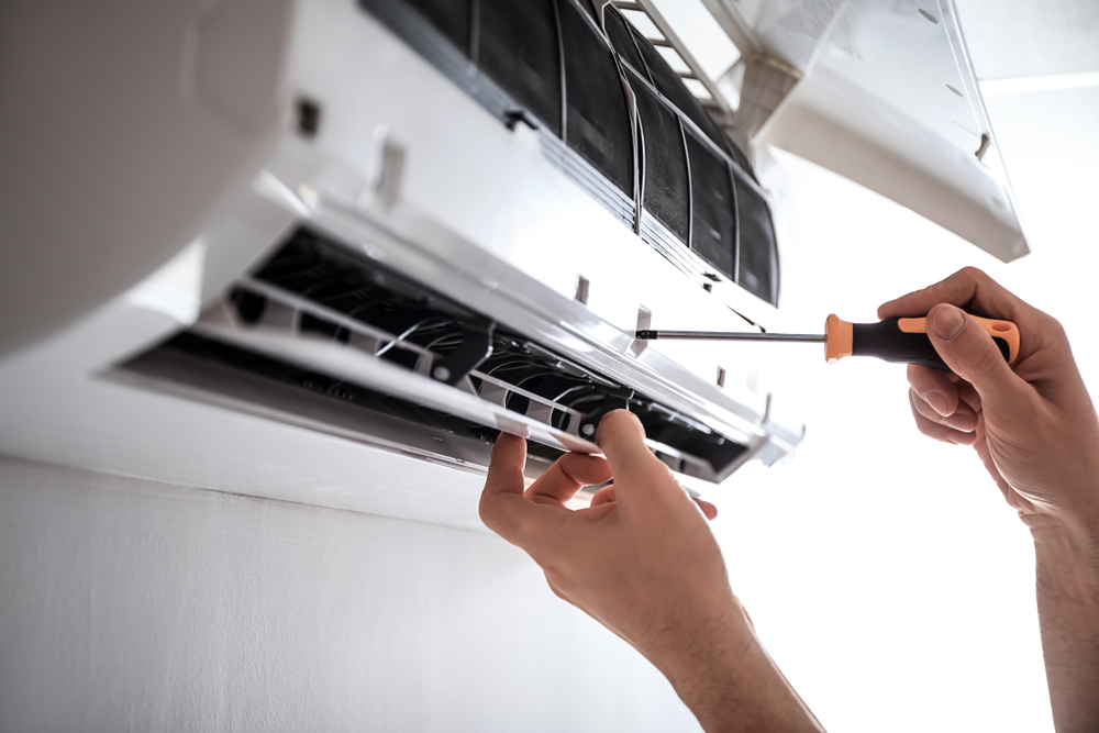 Mâini de electrician desfac un aparat de aer condiționat cu ajutorul unei șurubelnițe.